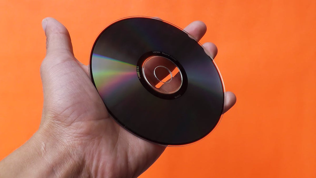 Person holding a CD carefully by the edges against an orange background.
