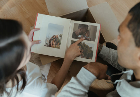 Two people sitting together and pointing at family photos inside a photo album.