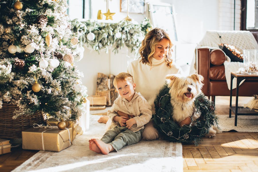 Mother, kid and a dog sitting by a decorated Christmas tree and wrapped presents.