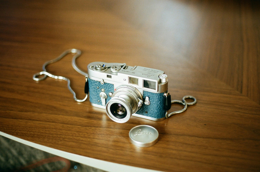 A vintage Leica camera with a blue leather grip resting on a wooden table.