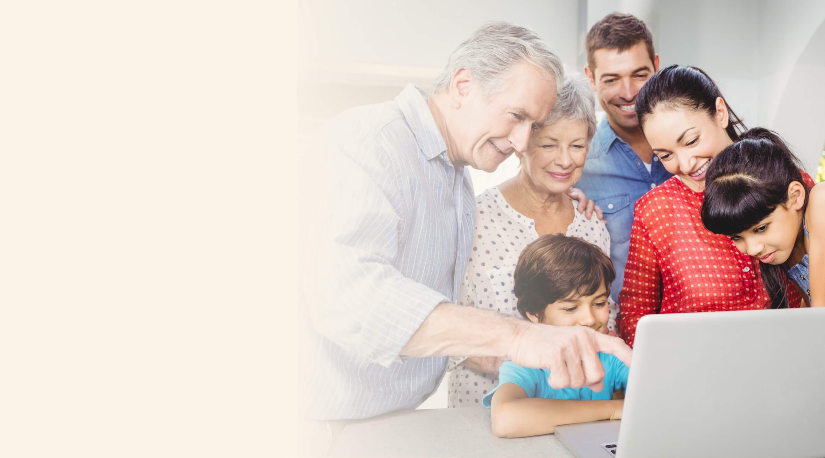 A multigenerational family, including grandparents, parents, and children, gathered around a laptop, smiling and looking at the screen.