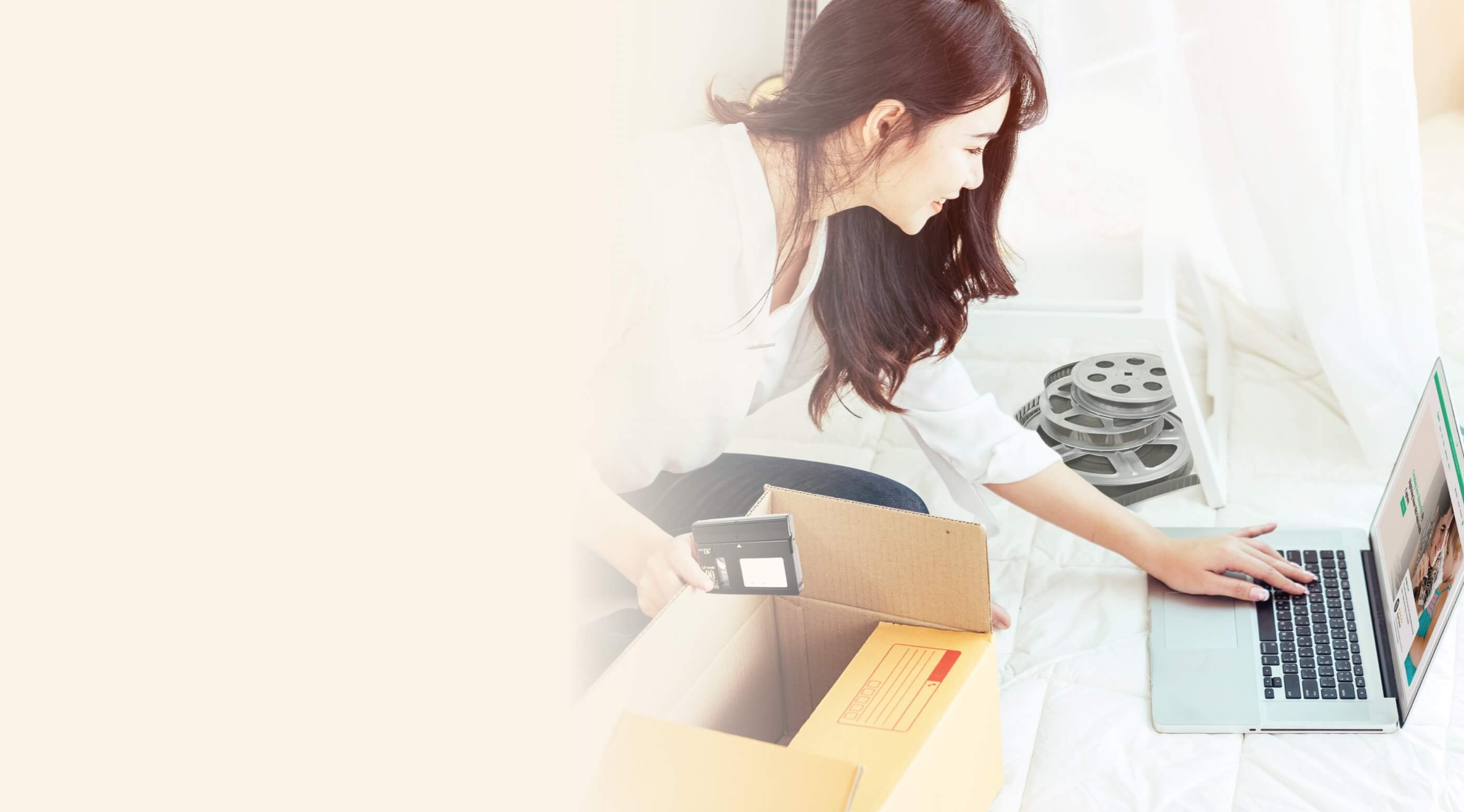 A woman sitting on the floor, scanning a film reel with a camera while using a laptop