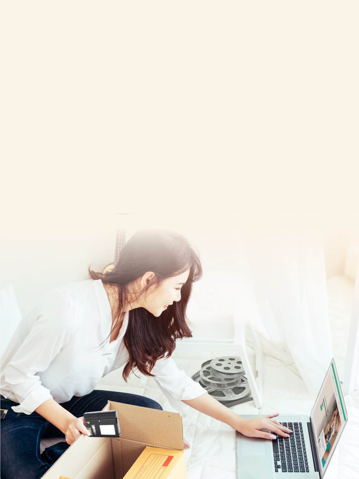 A woman sitting on the floor, scanning a film reel with a camera while using a laptop