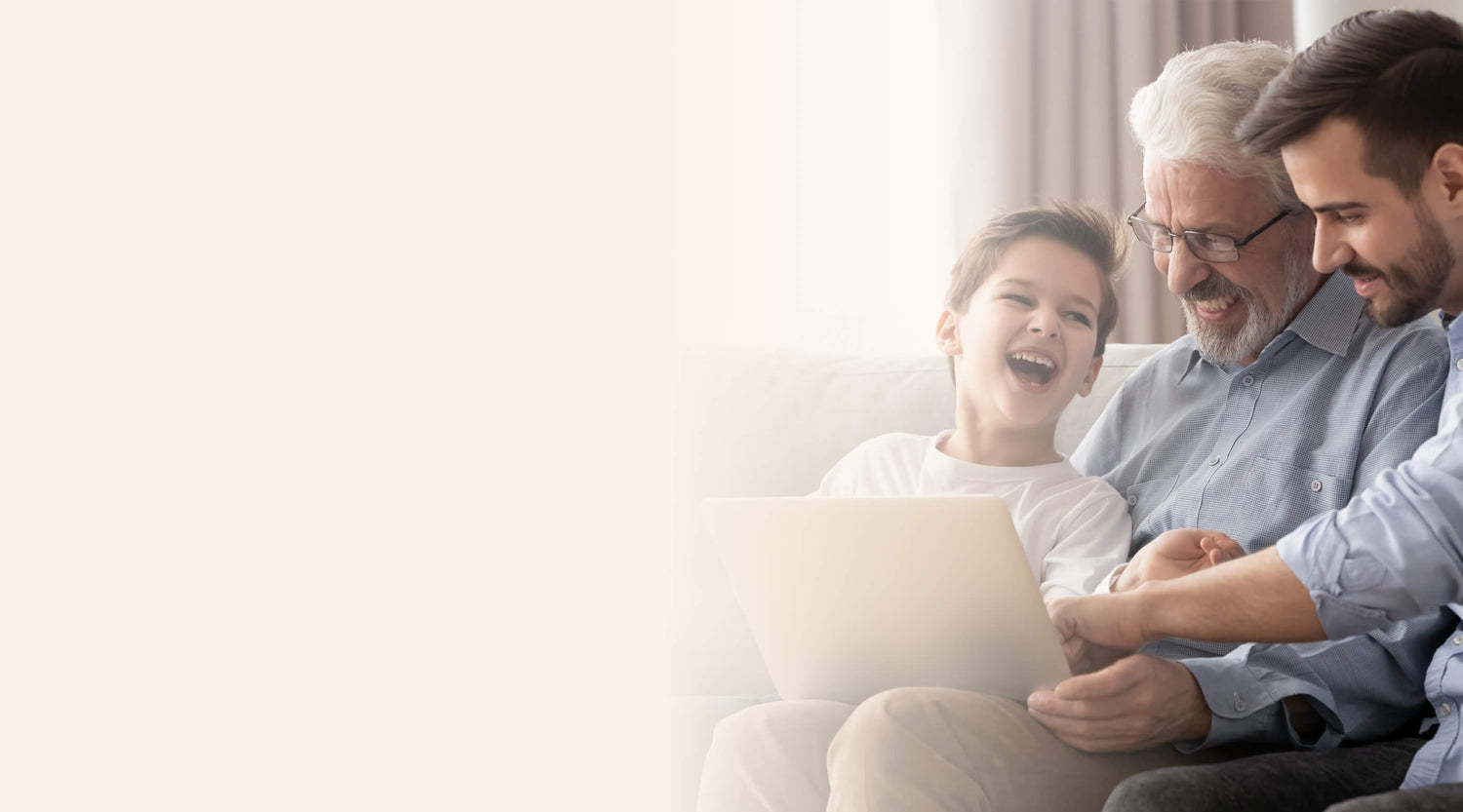 A grandfather, father, and son sitting together on a couch, smiling and looking at a laptop.