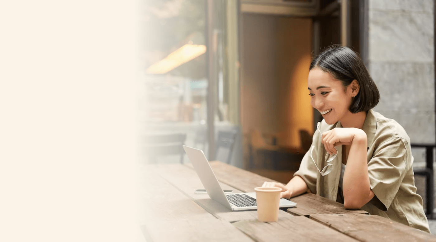 A woman sitting at a table, smiling while working on her laptop 