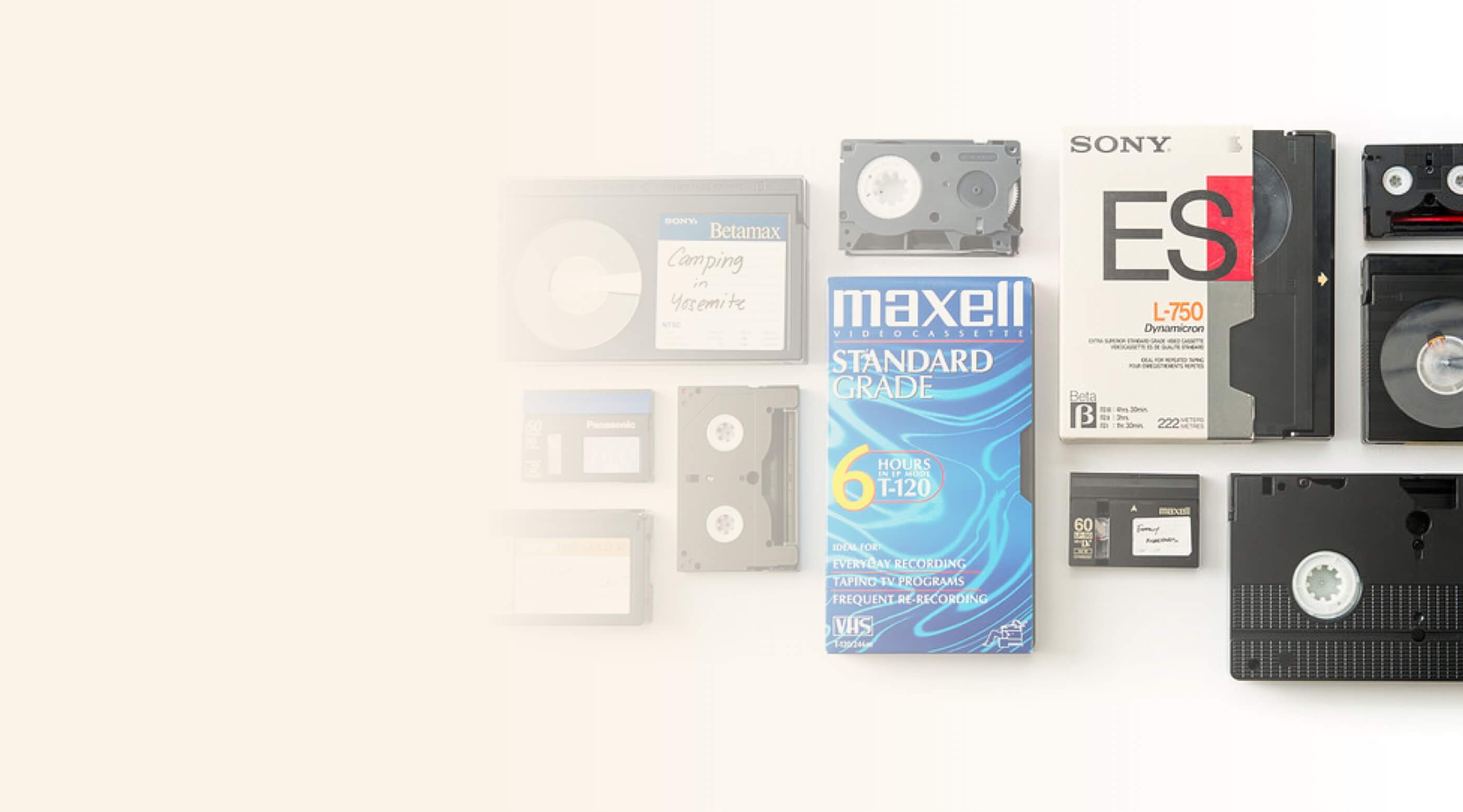 Various vintage video tapes including Betamax, VHS, and cassette tapes with labels and packaging on a light surface.