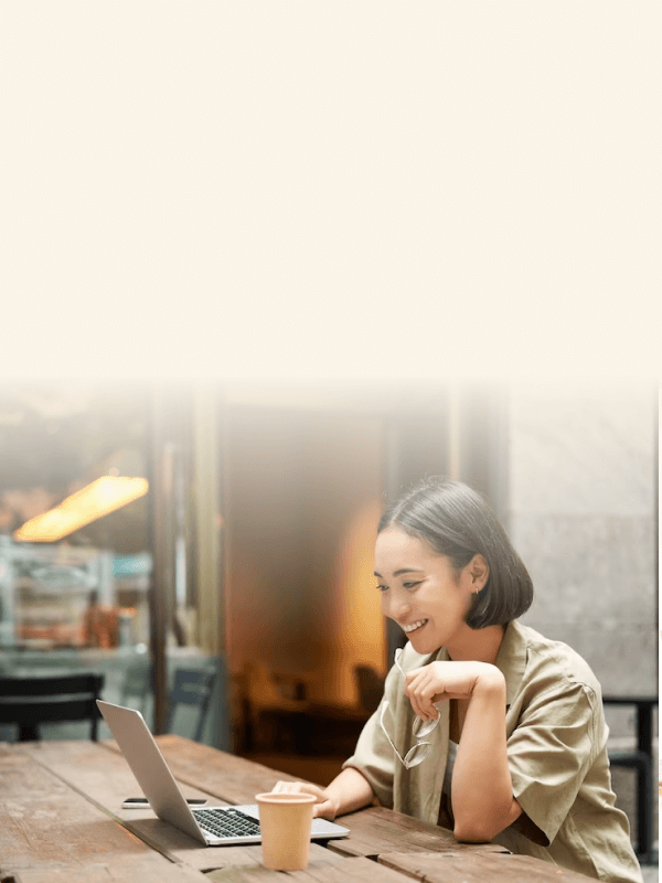 A woman sitting at a table, smiling while working on her laptop 